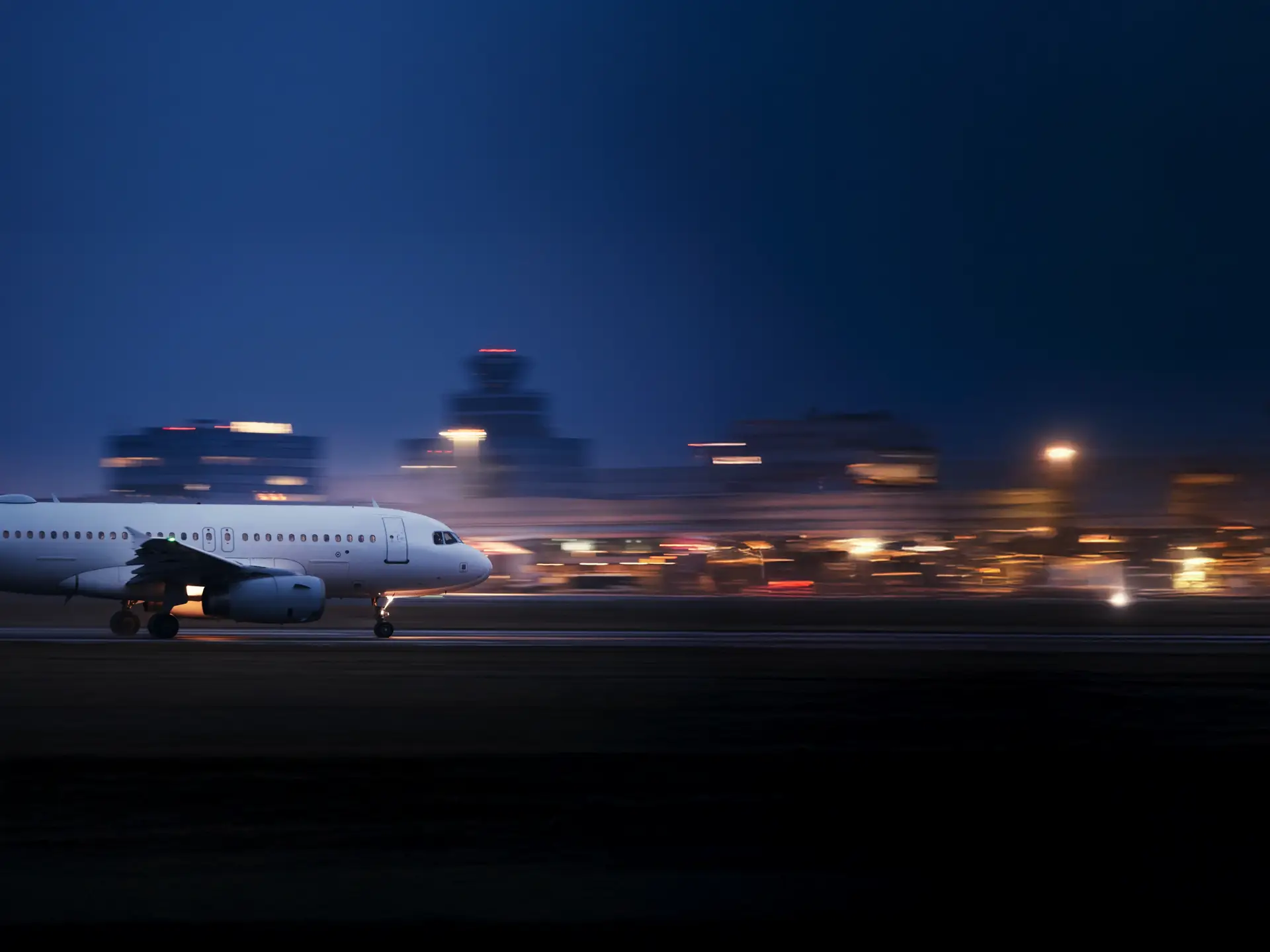 A white airplane speeds down a runway at night, with blurred city lights in the background.