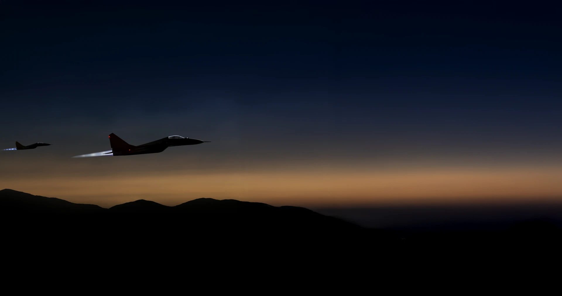 Two fighter jets flying at dusk against a dark sky, with silhouettes of hills visible below.